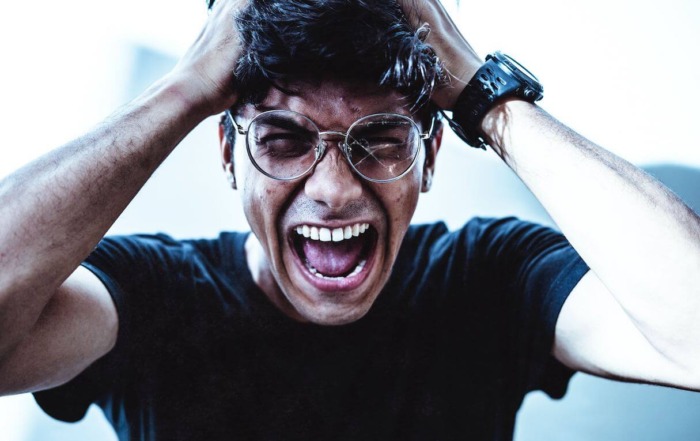 Image of a man with glasses, one lens cracked, with both hands on his head yelling in frustration. Post photo for "The Dire Consequences of Having a Narcissistic Parent" on Psychology Today by: Dr Stephanie Sarkis.